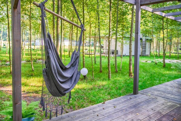 Una hamaca colgada de una estructura de madera en un área boscosa con una terraza de madera.