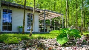 Una casa moderna con porche cubierto, rodeada de un jardín con diversas plantas y un camino de grava.