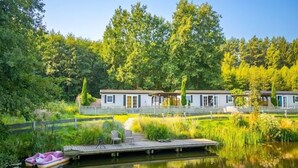 Propiedad frente al lago con un muelle, fila de cabañas y un bosque circundante.