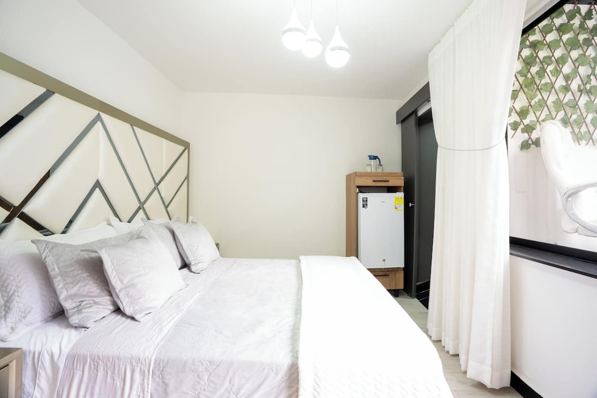 A bedroom with a bed, a wardrobe, a small desk, and a window with curtains.