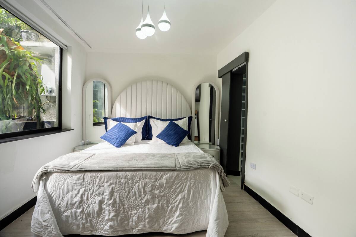 A bedroom with a bed, a window, a mirror, and a door.