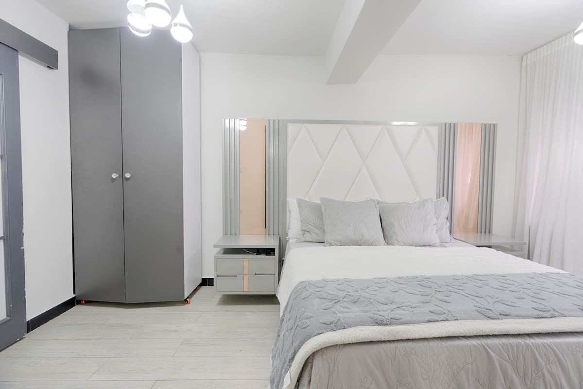 A bedroom with a bed, a wardrobe, a nightstand, and a mirror.