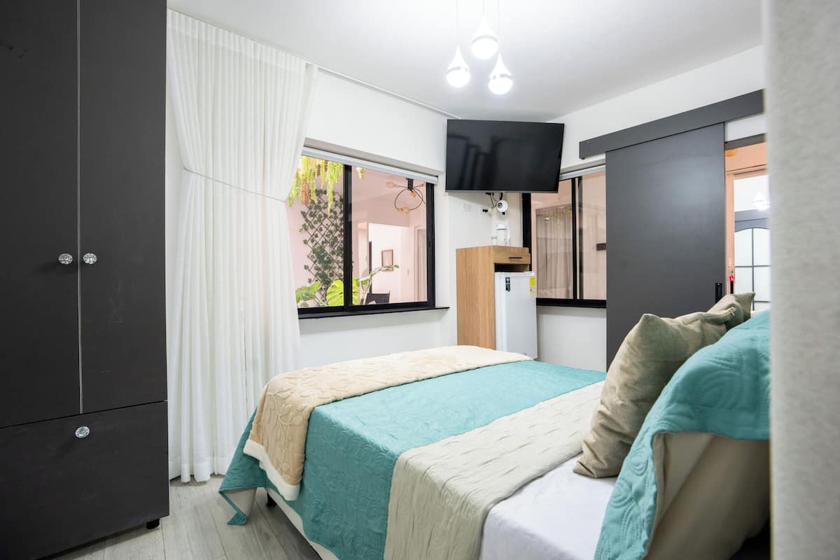 A bedroom with a bed, a wardrobe, a TV, and a window with curtains.