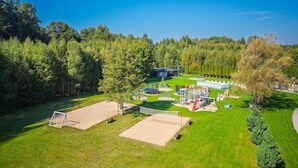 Hyvin hoidettu ulkoalue, jossa on lentopalloverkko, pieni leikkialue ja katettu oleskelualue.