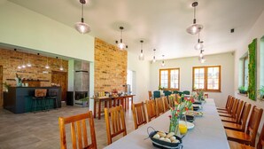 Un comedor amplio con una mesa larga, sillas de madera, lámparas colgantes y una pared de ladrillo.