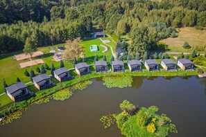 A lakeside property with multiple cabins arranged in a row along the water's edge, a playground, and a tennis court. - Single-story holiday home by the pond no. 9 (Darlowo)