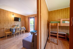 Ein Zimmer mit Holzwänden, einem Etagenbett, einem Schreibtisch mit Stühlen und einem Fernseher.