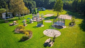 A playground with various play structures, a small building, and a grassy area with trees in the background. - Holiday cottage no. 2A with private jacuzzi (Darlowo)