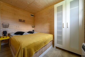 Una habitación de madera con cama, mesita de noche, lámpara, armario y estante con una cesta.