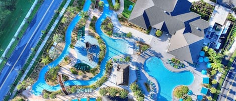 An aerial view of a resort with multiple swimming pools, a winding water feature, and a large building with a distinct roof pattern.