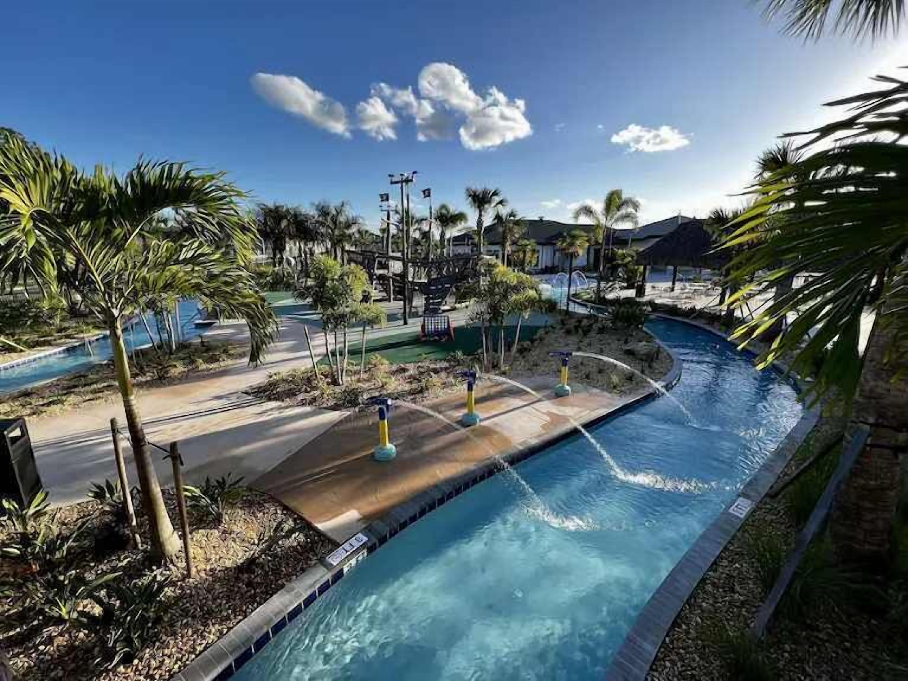 A swimming pool with a curved design, surrounded by palm trees and a clear sky.