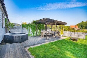 Un patio trasero con jacuzzi, terraza de madera, pérgola y mobiliario exterior.