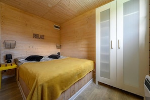 Ein Zimmer mit Holzboden, einem Bett, einem Nachttisch, einer Lampe, einem Kleiderschrank und einem Wandregal mit einem Korb.