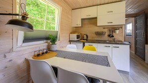 Une cuisine compacte aux murs en bois, dotée d’un plan de travail blanc et d’un coin repas avec une table et des chaises.