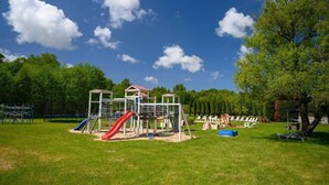 A playground with slides and climbing structures, surrounded by trees and grass. - Comfortable holiday home no. 2B with a fireplace (Darlowo)