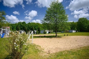 Ein Spielplatz mit Rutsche und umzäunter Fläche, umgeben von Bäumen und Häusern.