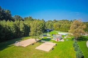 A large outdoor area with a volleyball net, a sandpit, and a covered seating area.