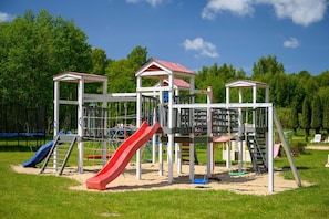 Ein Spielplatz mit einer roten Rutsche, Klettergerüsten und einem überdachten Spielhäuschen.