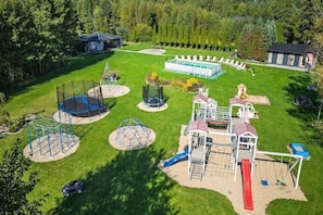 A playground with various play structures, a small building, and a pool area.