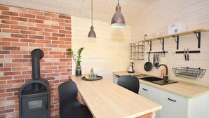 Une cuisine avec un mur en briques, un poêle à bois, une table en bois, des chaises noires, des luminaires suspendus et un évier.