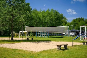 Ein Spielplatz mit einem Spielbereich unter Netz, einer Rutsche und einer Bank.