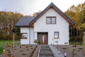 Ein modernes, zweistöckiges Haus mit einer symmetrischen Fassade, einem zentralen Eingang und einem geneigten Dach.