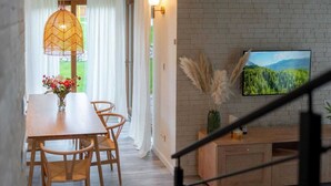 A dining area with a wooden table and chairs, a hanging light fixture, and a wall-mounted television displaying a forest scene. - Comfortable holiday villa, sauna, jacuzzi (Marcyporeba)