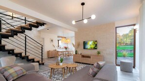 A modern living room with a staircase, a dining area, and a television mounted on a brick wall. - Comfortable holiday villa, sauna, jacuzzi (Marcyporeba)