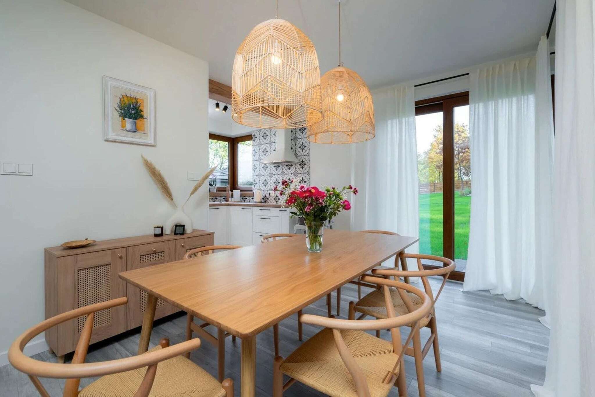 Et spiseområde med et træbord, fletstole og en vase med blomster.