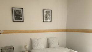 Una camera d'albergo con un letto, due quadri appesi al muro, una sedia, un comodino e una lampada.