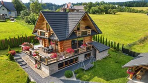 A log cabin with a balcony, a swing, and a garden with flowers.