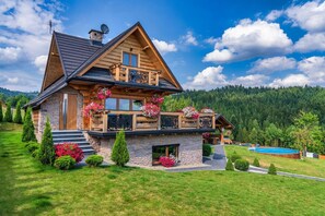 A two-story log cabin with a stone foundation, a balcony with flower boxes, and a swimming pool. - Luxury holiday villa, pool, sauna, jacuzzi (Nowy Targ)