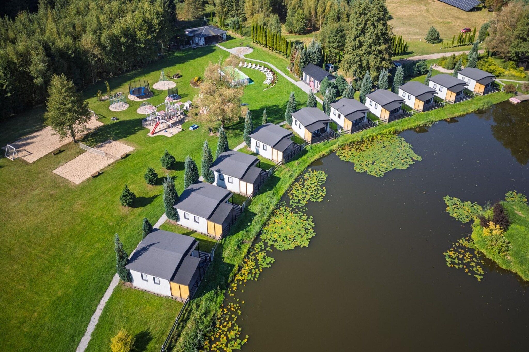 Un quartier résidentiel où les maisons sont alignées le long d’un plan d’eau sinueux, entouré de verdure et comprenant une aire de jeux.