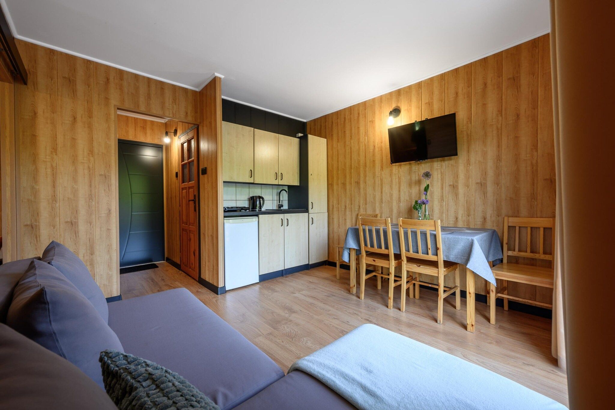 Un espace de vie compact comprenant un coin cuisine, un coin repas avec des chaises en bois et un canapé.