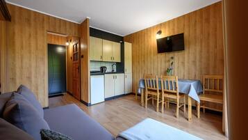 Un espace de vie compact comprenant un coin cuisine, un coin repas avec des chaises en bois et un canapé.
