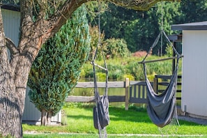 A hammock suspended from a tree in a backyard with a shed and a wooden fence in the background. - Single-story holiday home by the pond no. 6 (Darlowo)