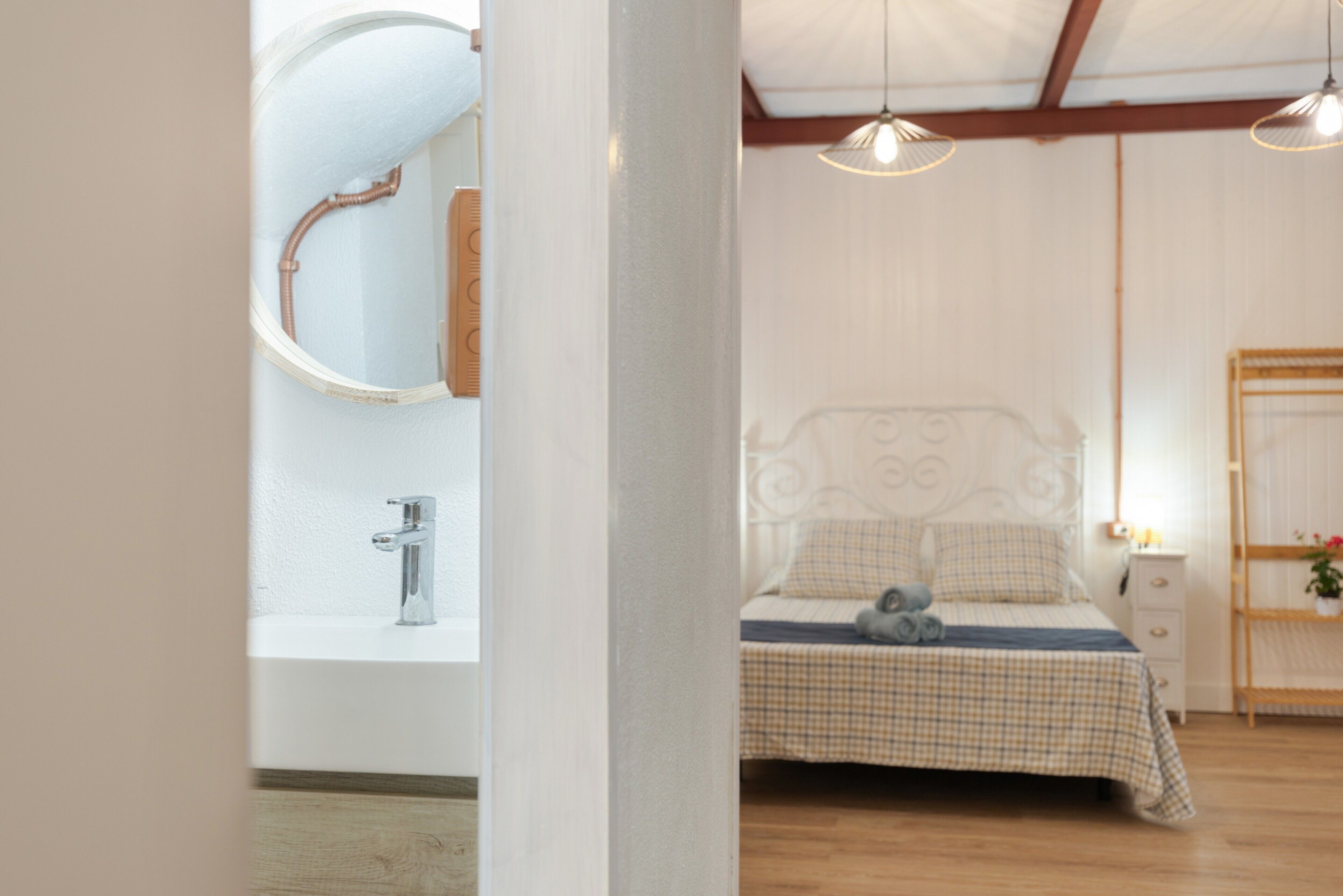 Een slaapkamer met een bed, een nachtkastje, een spiegel en een hanglamp.