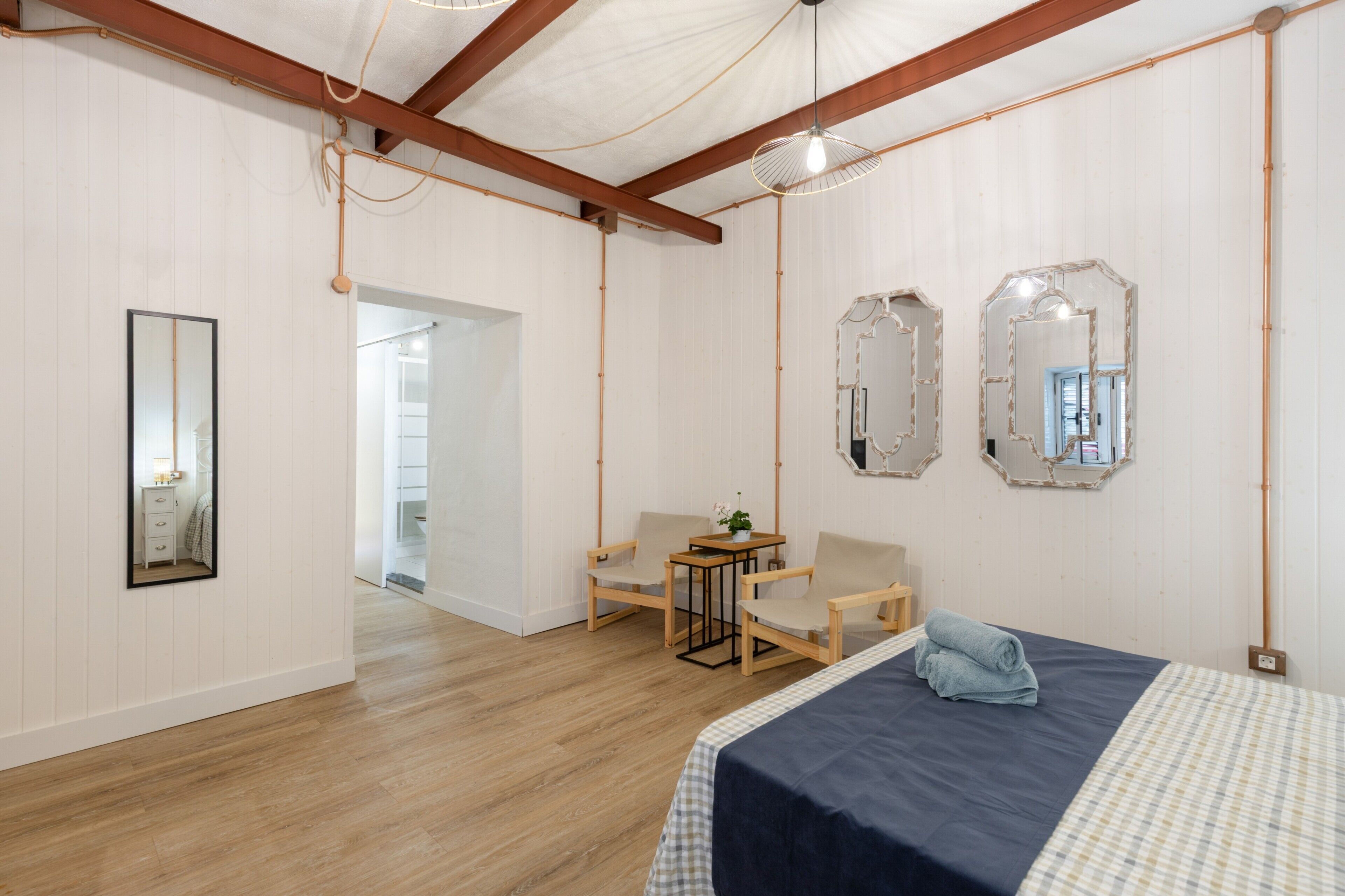 Une pièce comprenant un lit, deux chaises, une petite table et deux miroirs accrochés au mur.