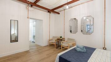 Une pièce comprenant un lit, deux chaises, une petite table et deux miroirs accrochés au mur.