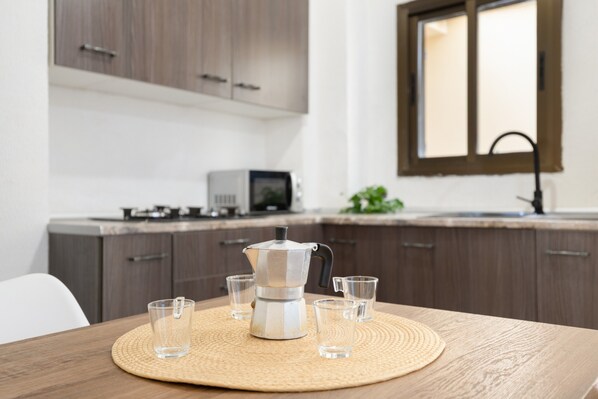 A kitchen with a coffee maker, four glasses, a woven placemat, and wooden cabinets.