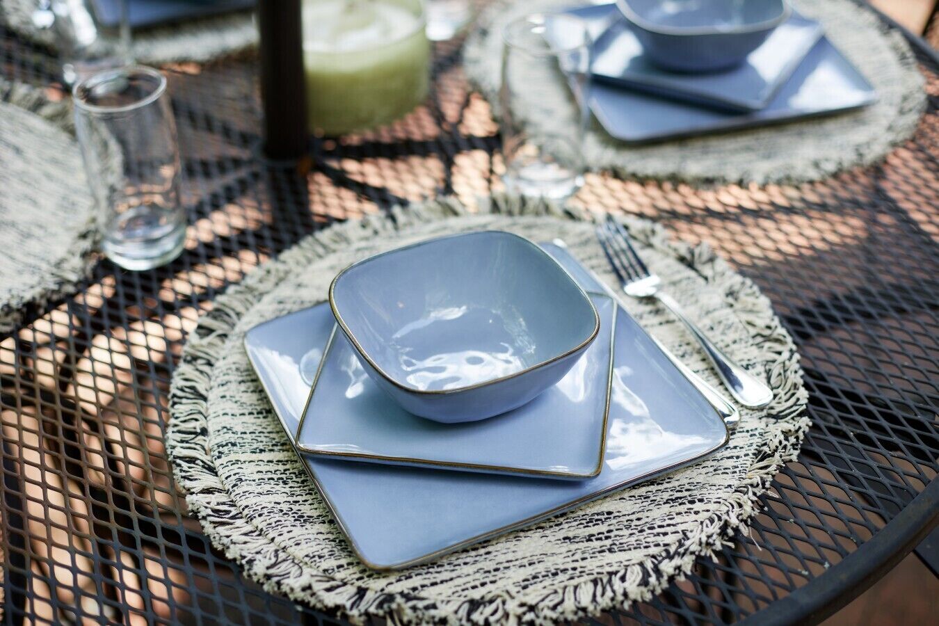 A table set with a blue bowl, square plates, and silverware on a woven placemat.