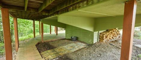 An outdoor covered area with a wooden deck, a brick pathway, and a pile of firewood.