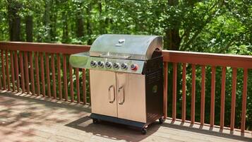 A portable barbecue grill on a wooden deck with a metal railing.