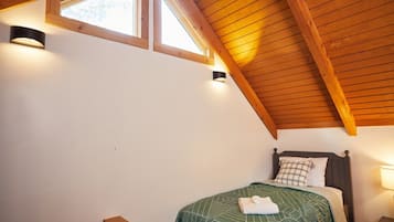 A bedroom with a sloped ceiling, a bed with a green patterned bedspread, and two wall-mounted lights.