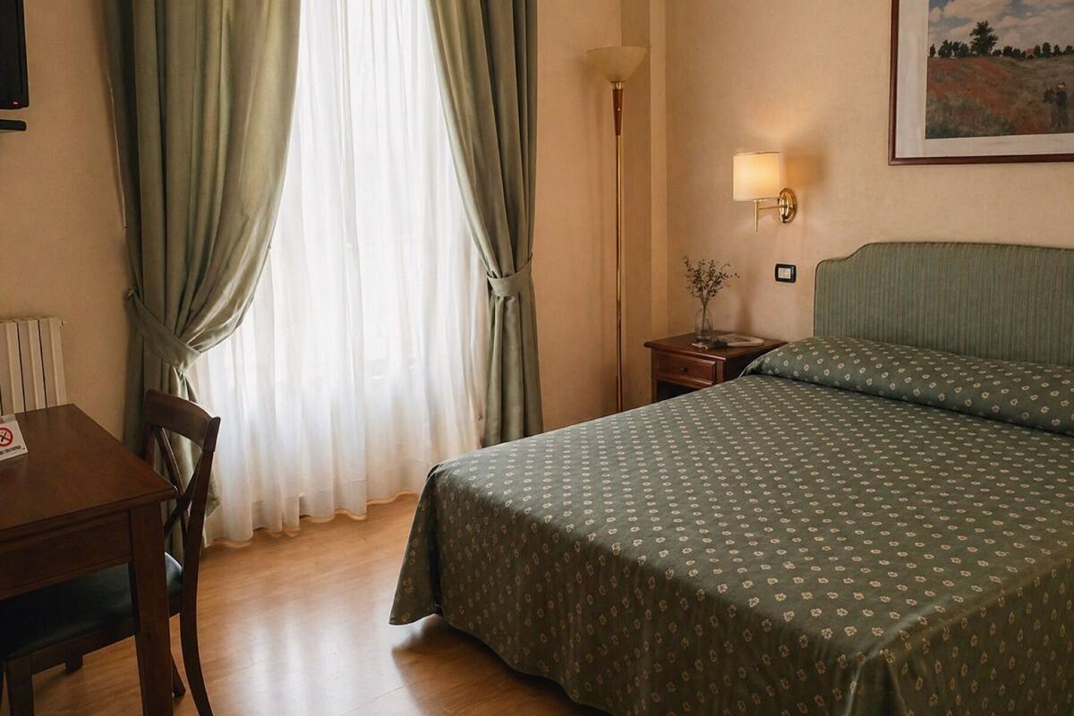 A hotel room with a bed, a desk, a chair, a nightstand, a lamp, and a painting on the wall.