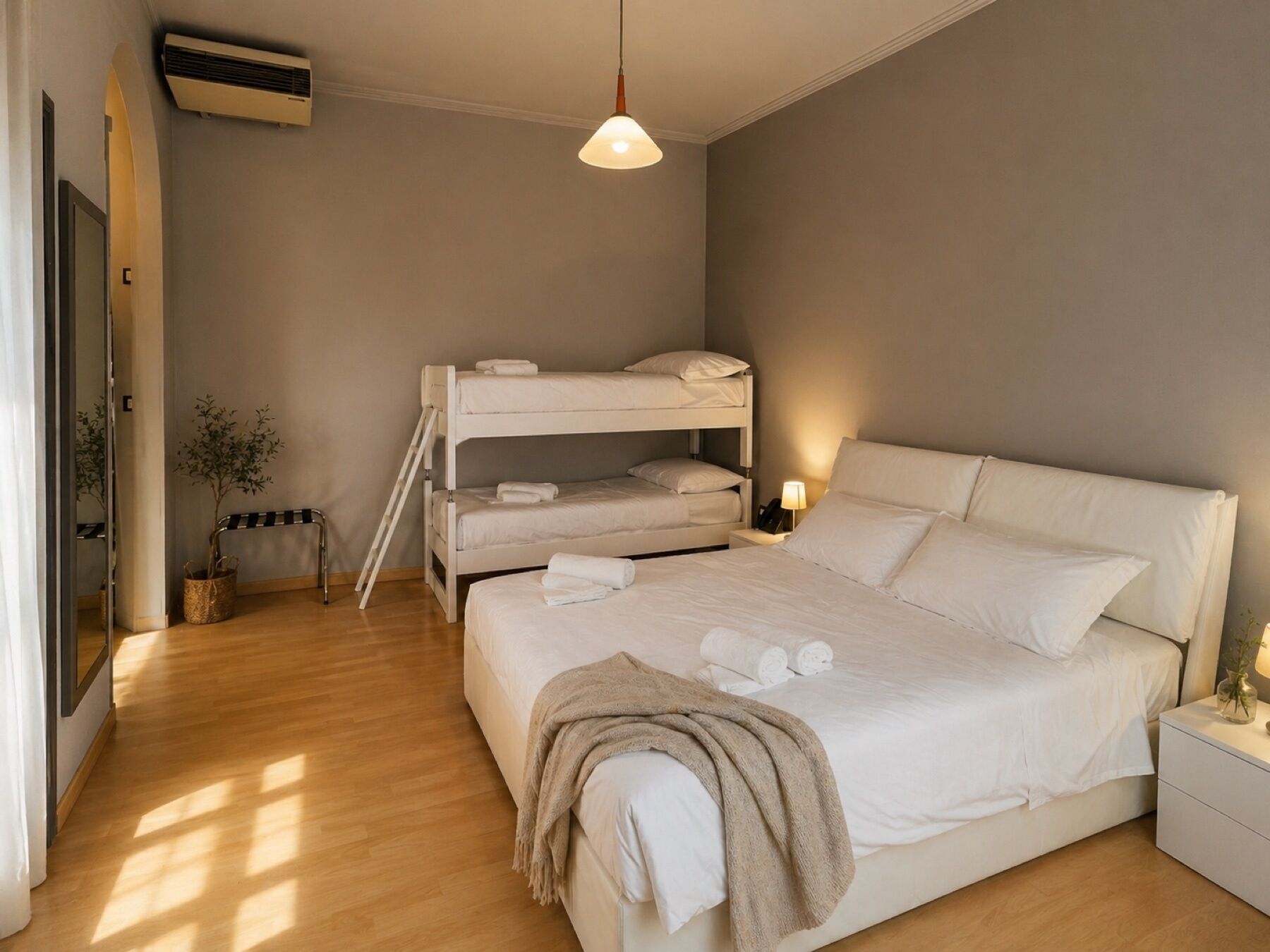 A bedroom with a bunk bed, a single bed, a bedside table with a lamp, a small plant, and a ceiling fan.