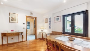 A dining area with a wooden table, chairs, a window with a view, and a wooden cabinet. - 'Terrazza Valtellina' Apartment with Mountain View, Shared Terrace, and Wi-Fi (Grosio)