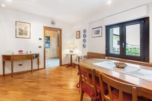 A dining area with a wooden table, chairs, a window with a view, and a wooden cabinet. - 'Terrazza Valtellina' Apartment with Mountain View, Shared Terrace, and Wi-Fi (Grosio)