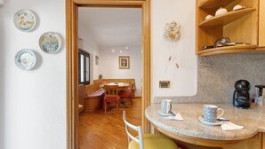 A kitchen with a round island, wooden cabinets, and a dining area with a table and chairs. - 'Terrazza Valtellina' Apartment with Mountain View, Shared Terrace, and Wi-Fi (Grosio)