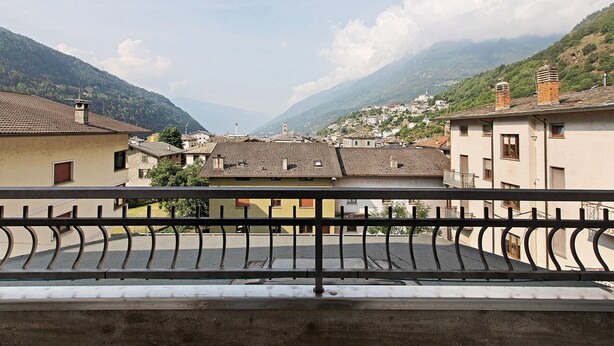 A balcony with a metal railing overlooking a town with buildings and mountains in the background. - 'Terrazza Valtellina' Apartment with Mountain View, Shared Terrace, and Wi-Fi (Grosio)